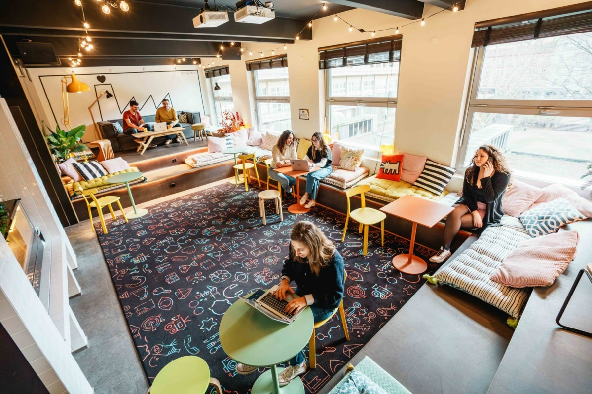 Plusieurs groupes de personnes en train de discuter et travailler sur des canapés ou tables de couleurs.