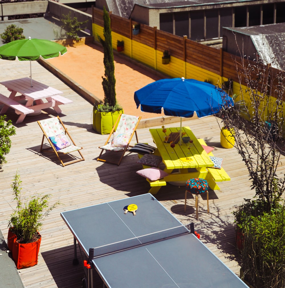 Rooftop avec table de ping-pong, transats et parasols colorés.